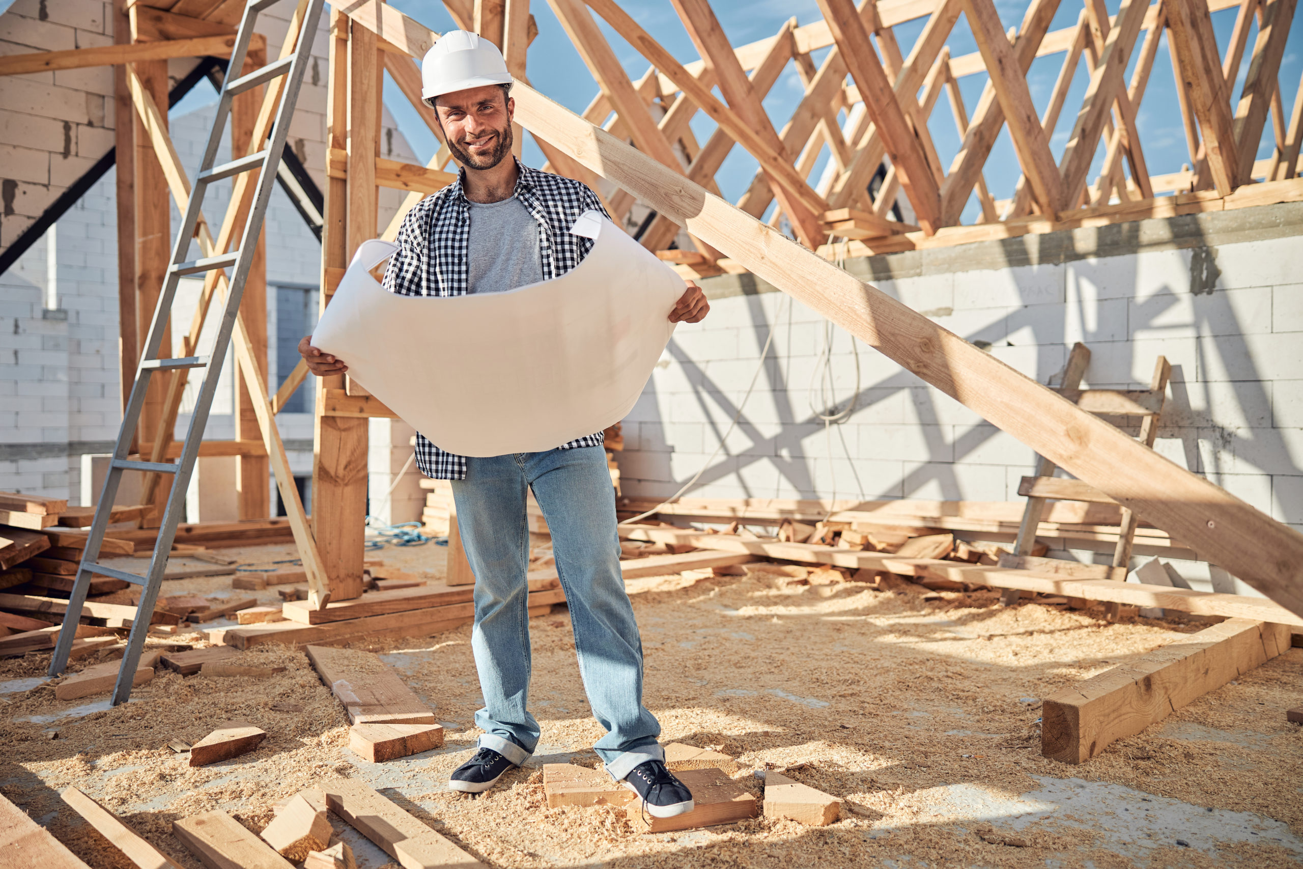 Joyful young man in a hardhat holding a building plan