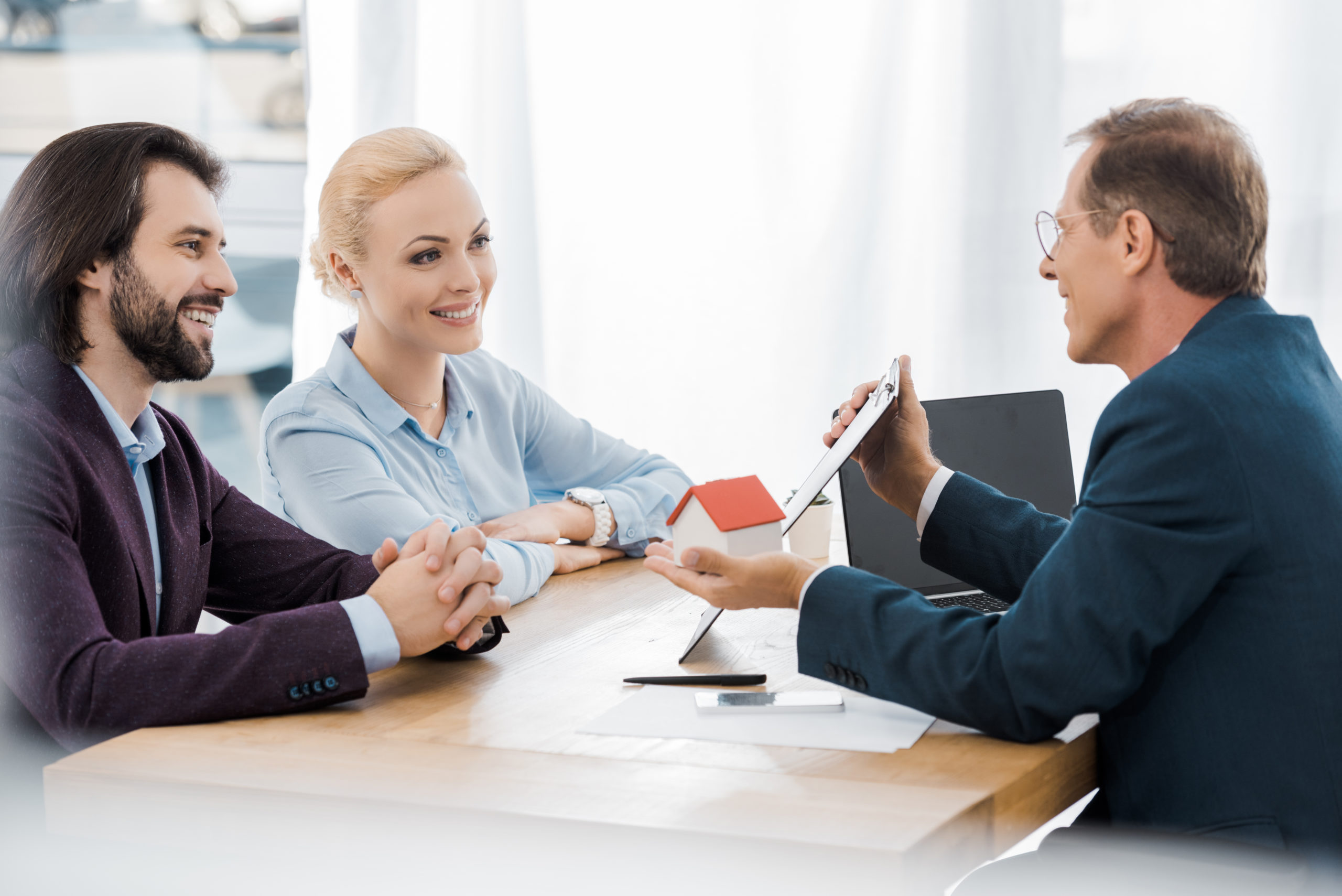 adult smiling insurance agent showing contract and house model to young couple in office