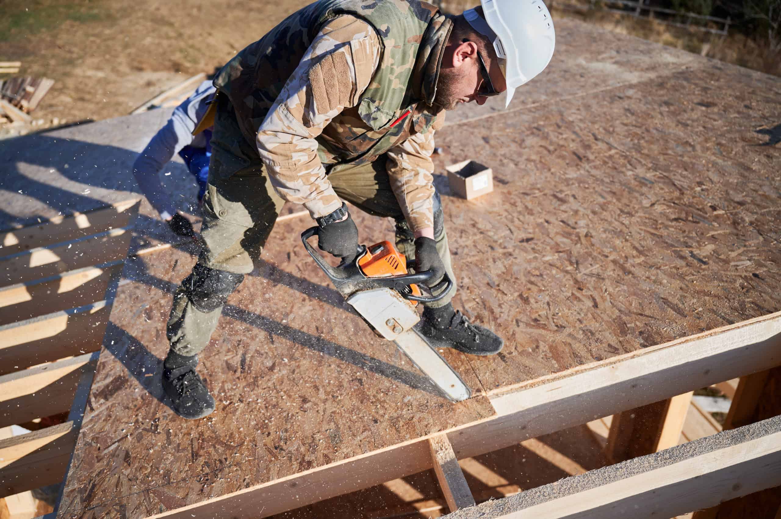 Carpenter using chainsaw for cutting OSB board for building wooden frame house. Carpenter using chainsaw for cutting OSB board for building wooden frame house.