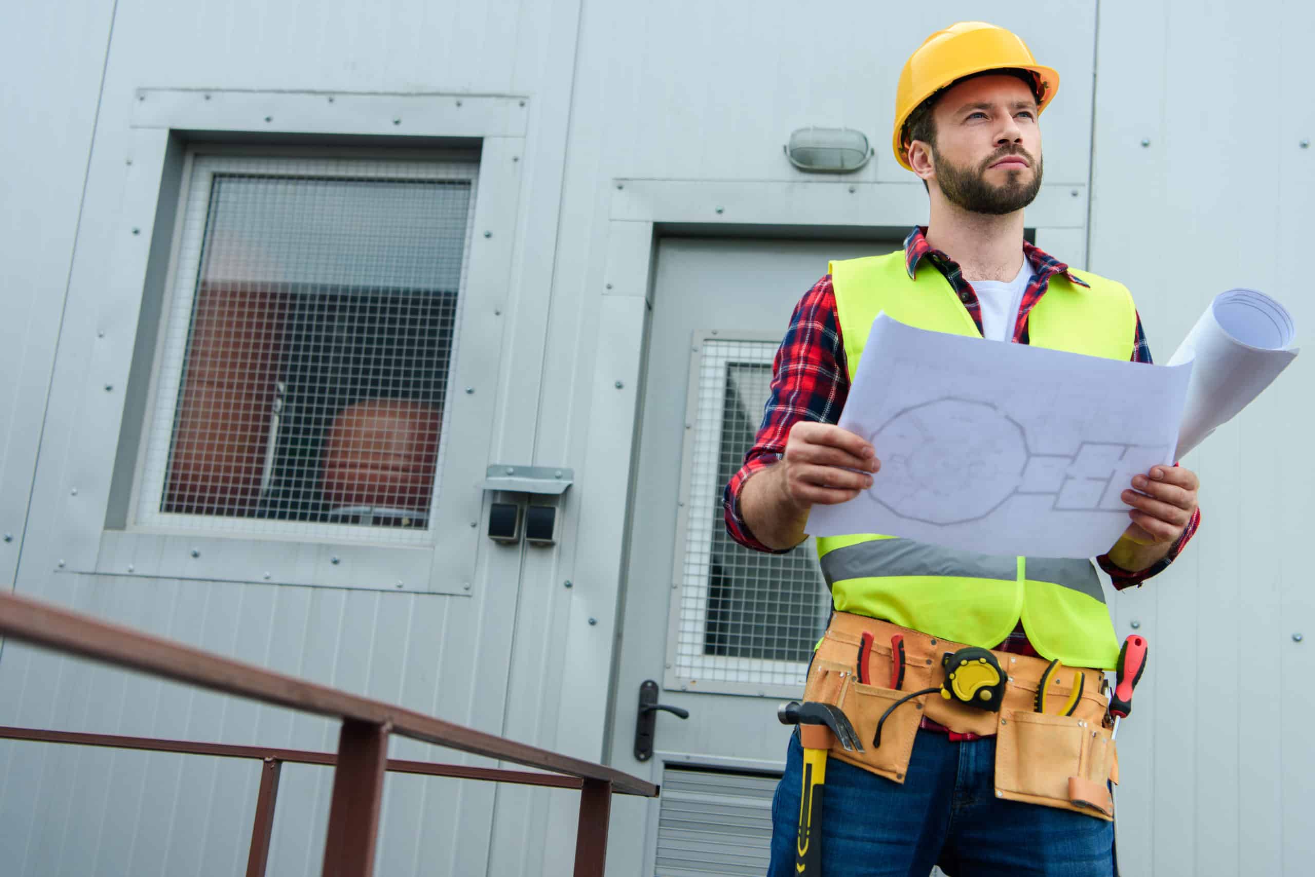 male professional engineer in safety vest and helmet working with blueprints male professional engineer in safety vest and helmet working with blueprints