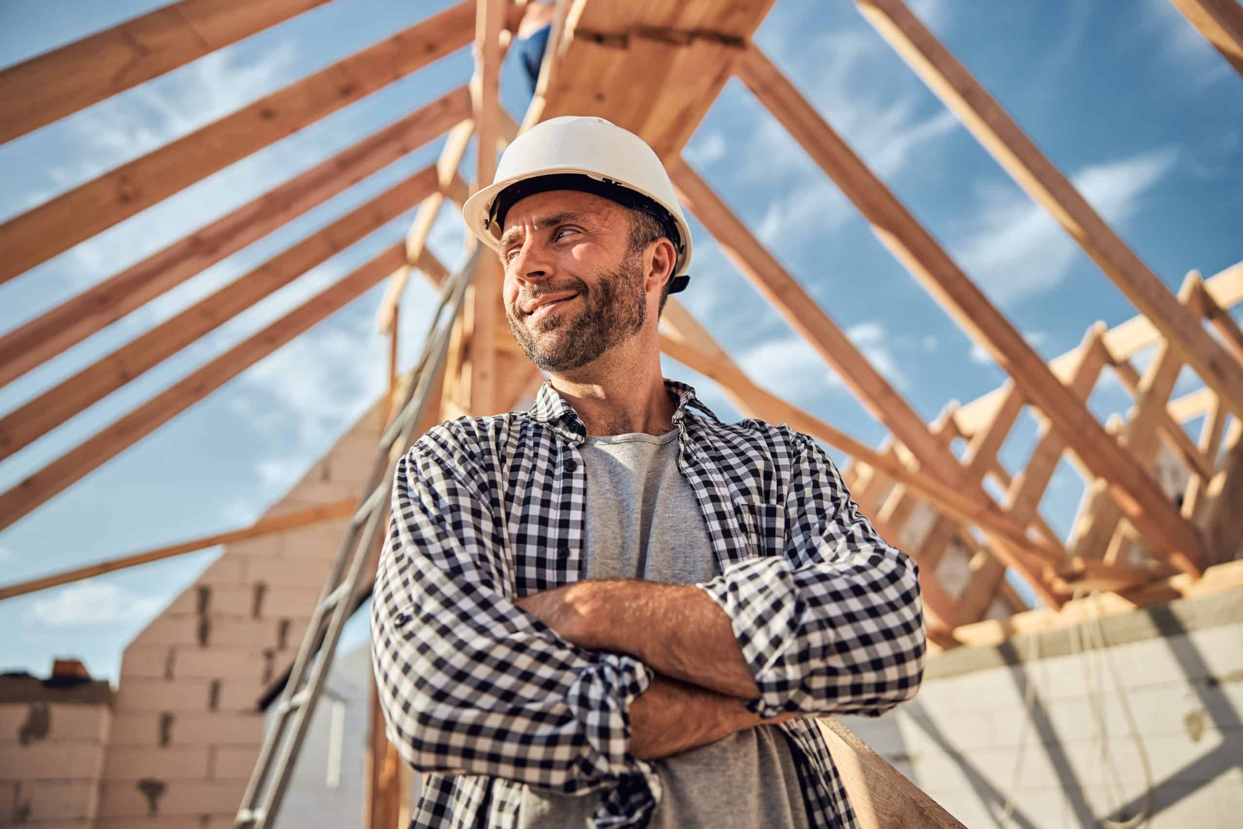 Pleased man in a hard hat posing under a wooden roof Construction Worker