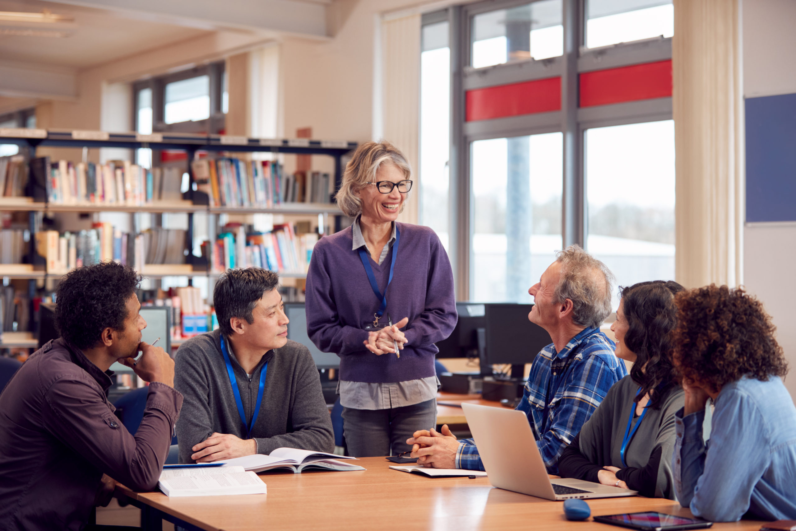 Teacher With Group Of Mature Adult Students In Class Sit Around Table And Work In College Library Teacher With Group Of Mature Adult Students In Class Sit Around Table And Work In College Library