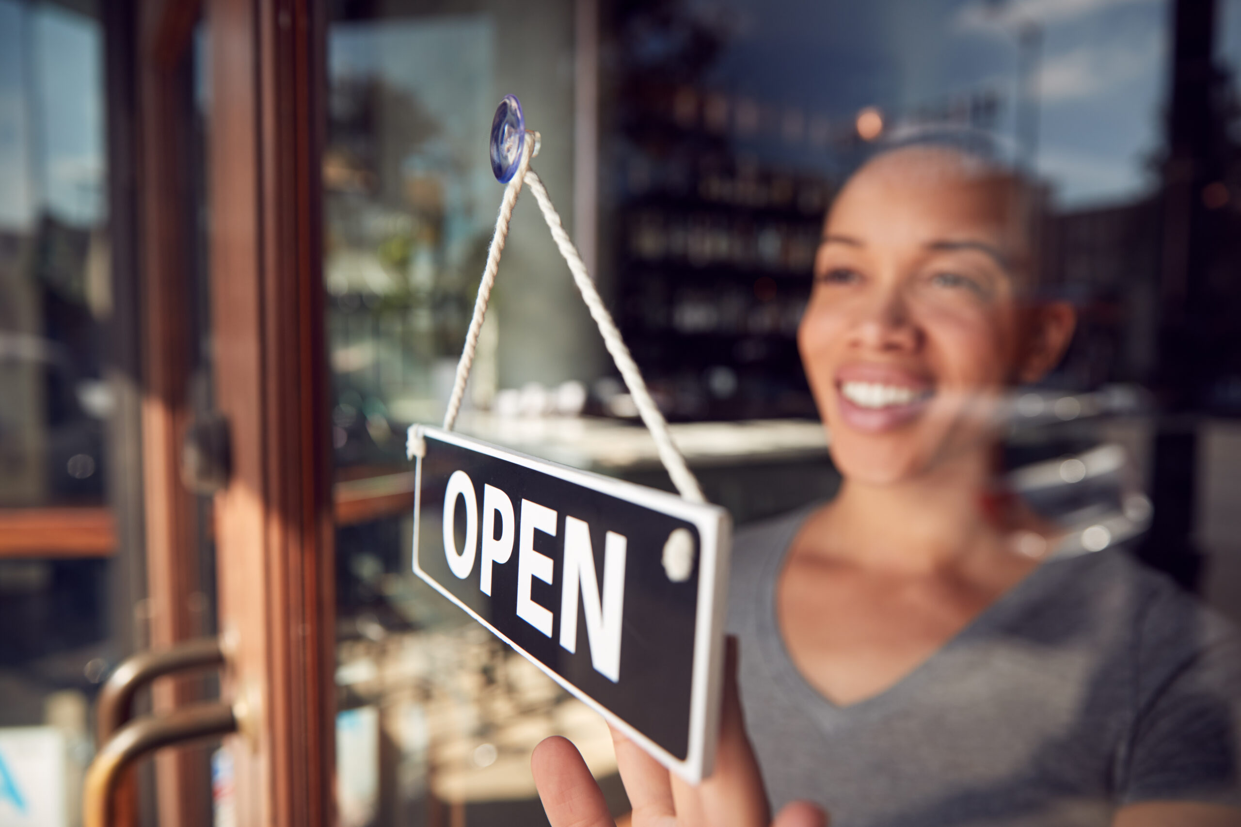 Female Owner Of Start Up Coffee Shop Or Restaurant Turning Round Open Sign On Door Female Owner Of Start Up Coffee Shop Or Restaurant Turning Round Open Sign On Door