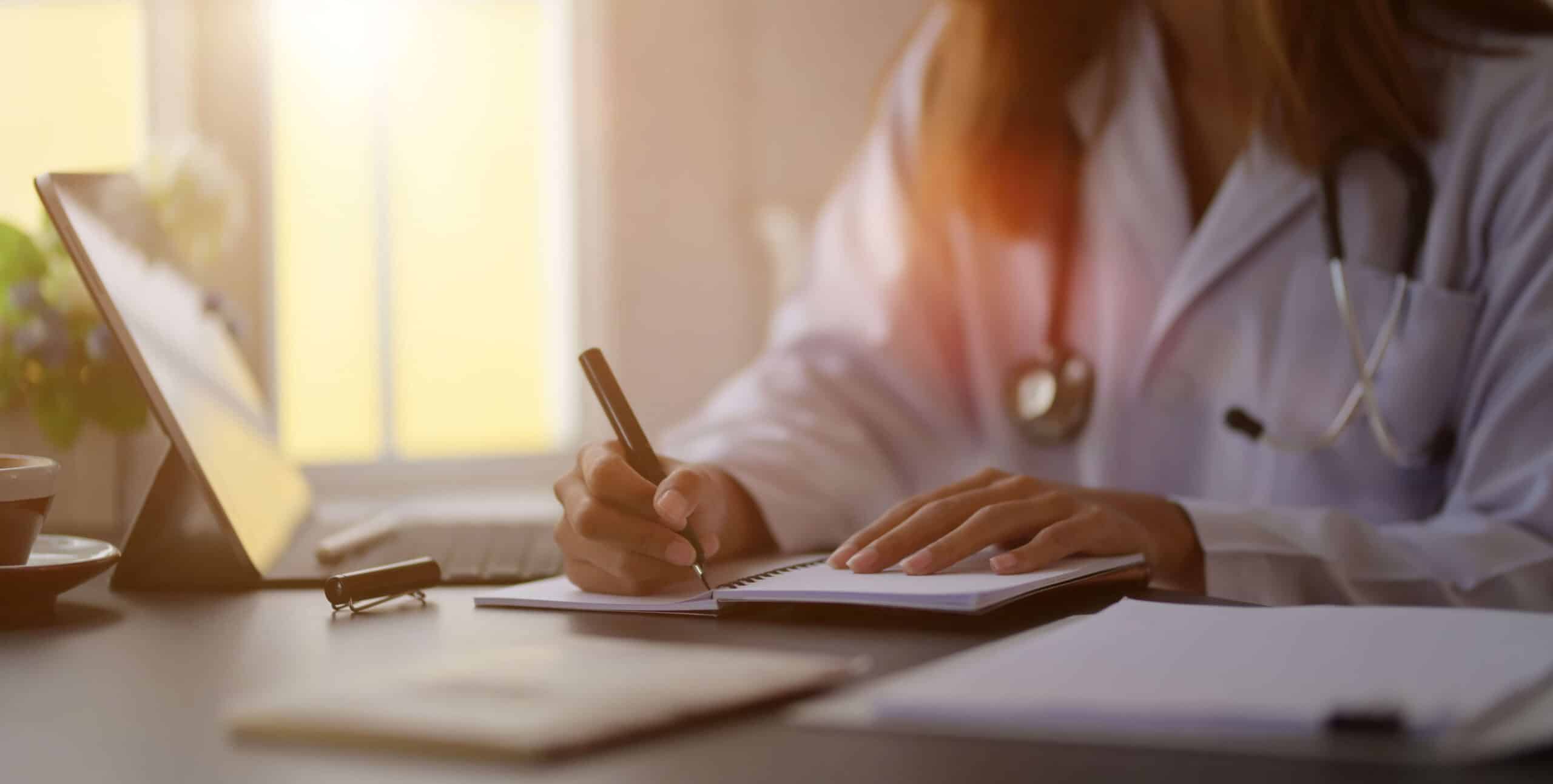 A woman Writing on Notepad with ipad open on other side